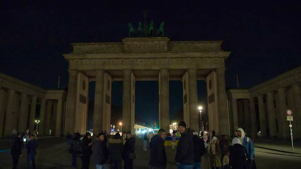 dpatopbilder - People stand in front of the dark Brandenburg Gate. With the worldwide "Earth Hour" campaign, the environmental protection organization WWF wants to set an example for more climate protection. Photo: Paul Zinken/dpa