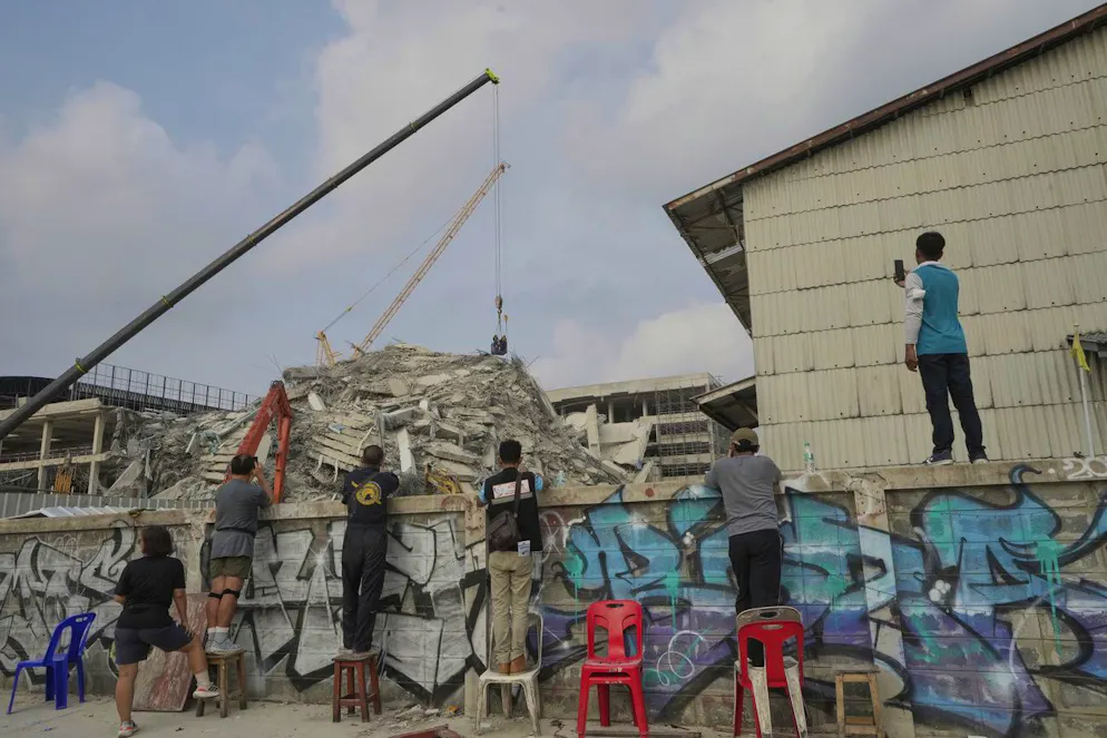 Zaungäste beobachten heute die Rettungsarbeiten in Bangkok bei einem eingestürzten Hochhaus.