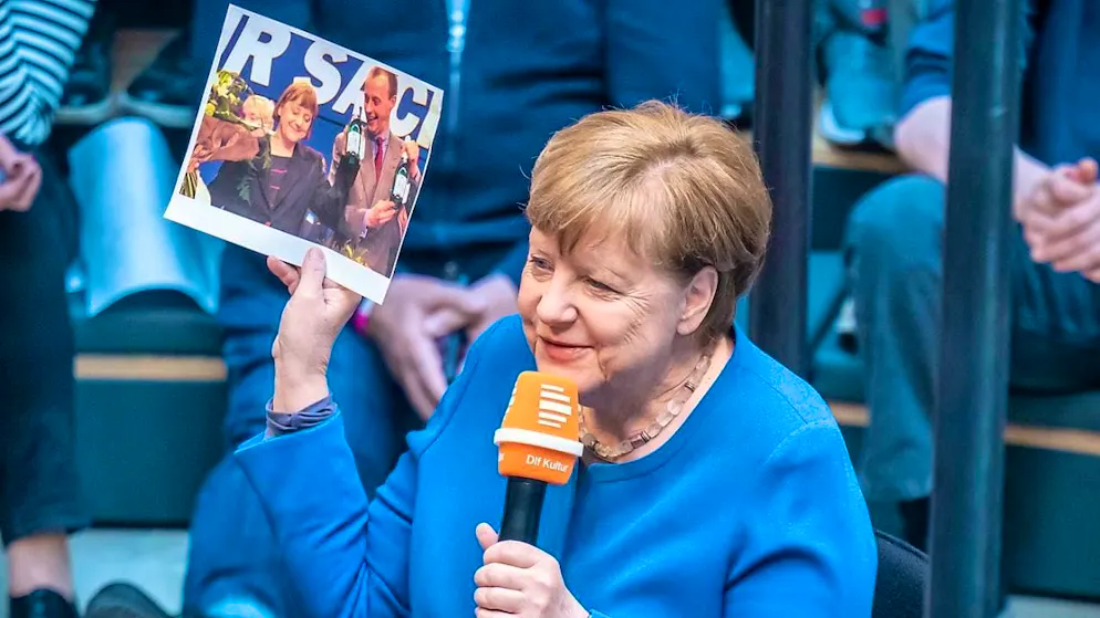 Former German Chancellor Angela Merkel is a guest on Deutschlandfunk's live radio show "Studio 9" at the Humboldt Forum and looks at an old photo of her and Friedrich Merz. Photo: Michael Kappeler/dpa