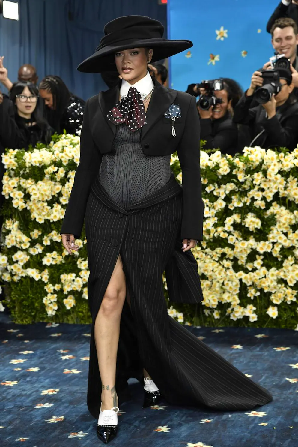 Rihanna – le défilé de tenues de grossesse a commencé!.  Ni son immense chapeau, ni sa cravate en satin à pois n’ont détourné les regards de l’heureuse nouvelle, subtilement mise en scène sous ce bustier.
