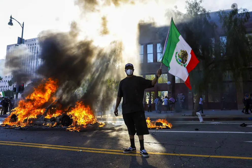 epa12165554 Un manifestant brandissant un drapeau mexicain observe plusieurs voitures en feu lors de manifestations contre les rafles de migrants à Los Angeles, en Californie, aux États-Unis, le 8 juin 2025. Le président américain Donald Trump a déployé 2 000 soldats de la Garde nationale, bien que l'État de Californie n'ait pas demandé d'aide supplémentaire, à la suite des importantes manifestations contre les raids anti-immigration menés ces derniers jours dans la région de Los Angeles. EPA/CAROLINE BREHMAN