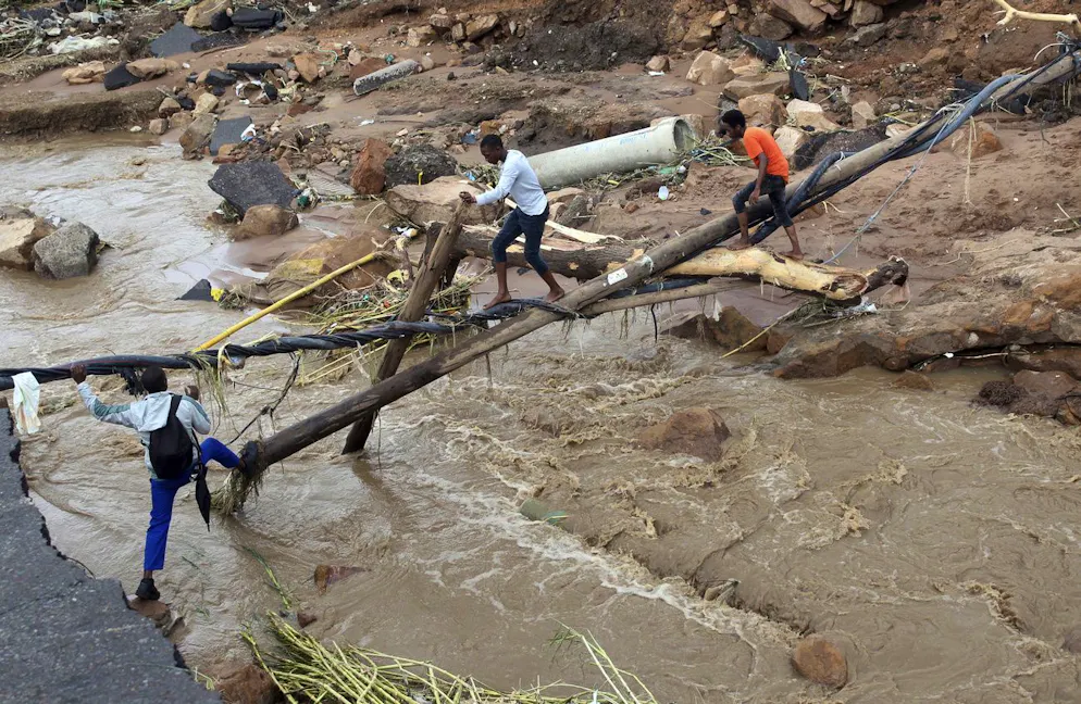 Des personnes traversent un pont de fortune au-dessus d'une rivière, après qu'un pont a été emporté par les eaux à Ntuzuma, près de Durban, en Afrique du Sud.