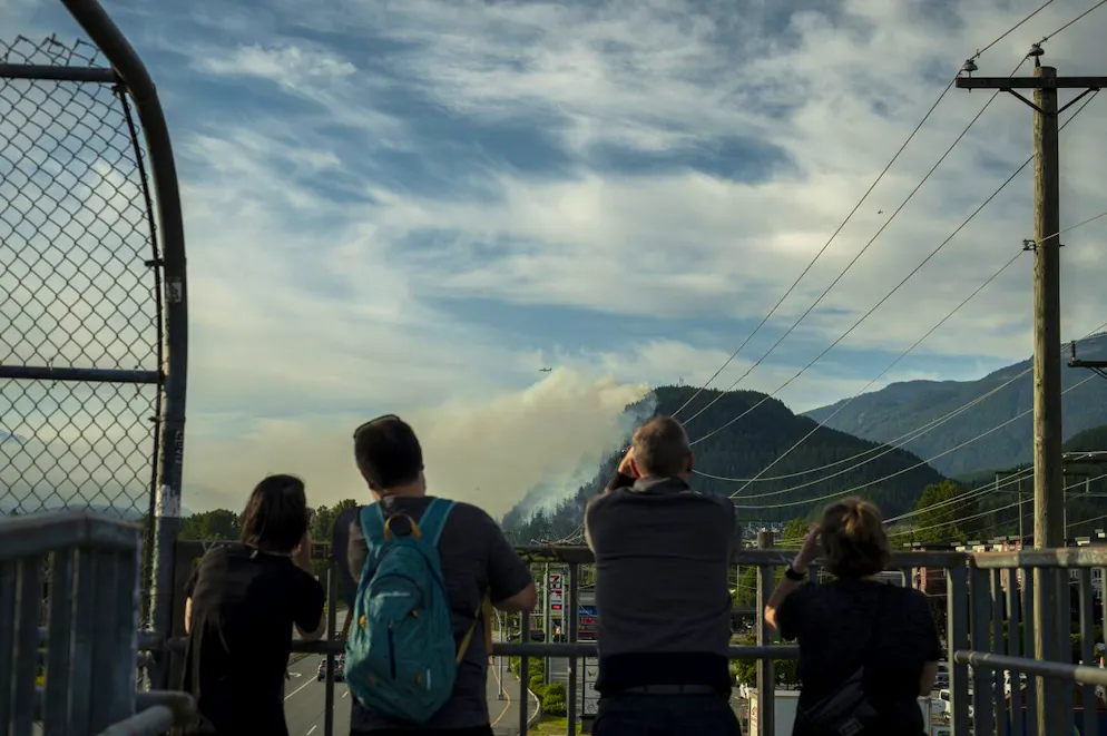 Des gens observent l'incendie de Dryden Creek depuis un pont piétonnier à Squamish, en Colombie-Britannique, le mardi 10 juin 2025. (Tijana Martin/La Presse Canadienne via AP)