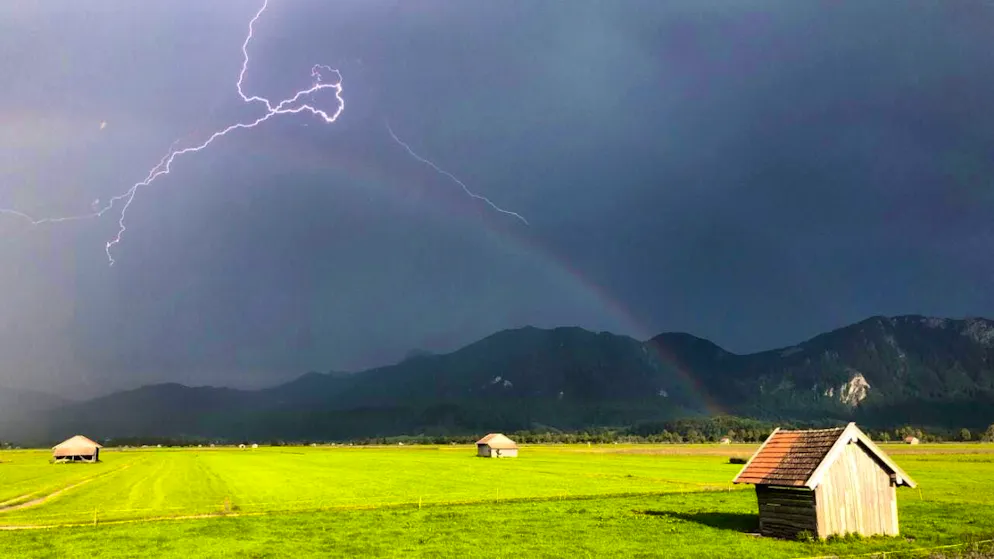Lightning flashes over the foothills of the Bavarian Alps, while a rainbow is visible over a pasture. +++ dpa-Bildfunk +++