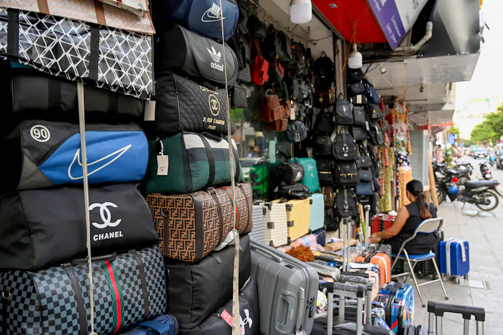 Cette photo prise le 10 juin 2025 montre des sacs portant les logos de marques de mode internationales en vente devant un magasin à Hanoï. Depuis que les États-Unis ont accusé le Vietnam d'être une plaque tournante de la contrefaçon, Tran Le Chi a de plus en plus de mal à trouver ses faux t-shirts Chanel, ses lunettes de soleil Gucci et ses sacs à main Louis Vuitton préférés. (Photo par Nhac NGUYEN / AFP) / POUR ACCOMPAGNER « VIETNAM-ÉTATS-UNIS-FRAUDE COMMERCIALE-VÊTEMENTS, FOCUS » PAR TRAN THI MINH HA ET ALICE PHILIPSON