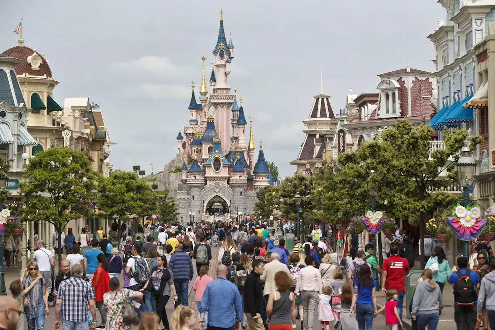 FILE - In this May 12, 2015, file photo, visitors walk near Sleeping Beauty's Castle at Disneyland Paris, in Marne la Vallee, east of Paris. Disney brought its vision of Americana to France with the opening of Disneyland Paris and Walt Disney Studios Park in 1992. To please France, French is the main language for the park, which includes French and European-themed attractions. Mickey and Donald retained their names, but Goofy is called Dingo and Snow White and the Seven Dwarfs are Blanche Neige et Les Sept Nains. (AP Photo/Michel Euler, File)
