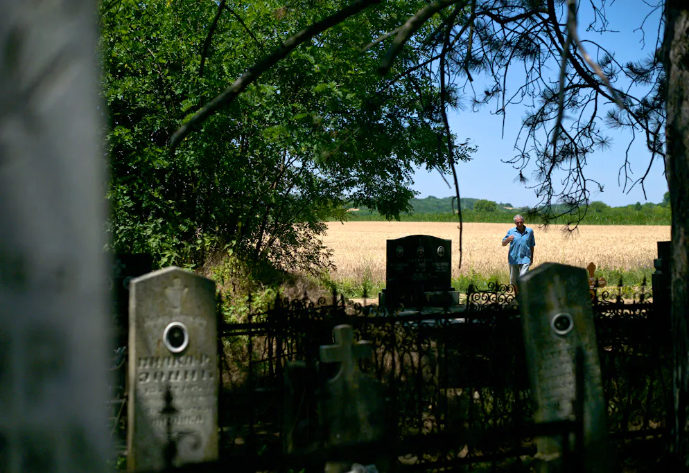 Mirko Bogicevic, 68 ans, habitant local et chroniqueur du village, passe devant les cimetières de Kisiljevo le 23 juin 2025. La Roumanie est connue comme le pays de Dracula, mais c'est en Serbie, il y a 300 ans, qu'un vampire aurait été vu pour la première fois. Aujourd'hui, le petit village de Kisiljevo aimerait bien récupérer son titre de berceau des vampires, et les touristes qui vont avec. Pour retrouver Petar Blagojevic, le premier des vampires, il faut entrer dans un petit cimetière coincé entre trois champs de maïs et un lac, à une centaine de kilomètres à l'est de Belgrade. Sous une chaleur étouffante, on marche derrière les tombes pour découvrir de vieilles pierres tombales sous un tas de broussailles. (Photo : OLIVER BUNIC / AFP)