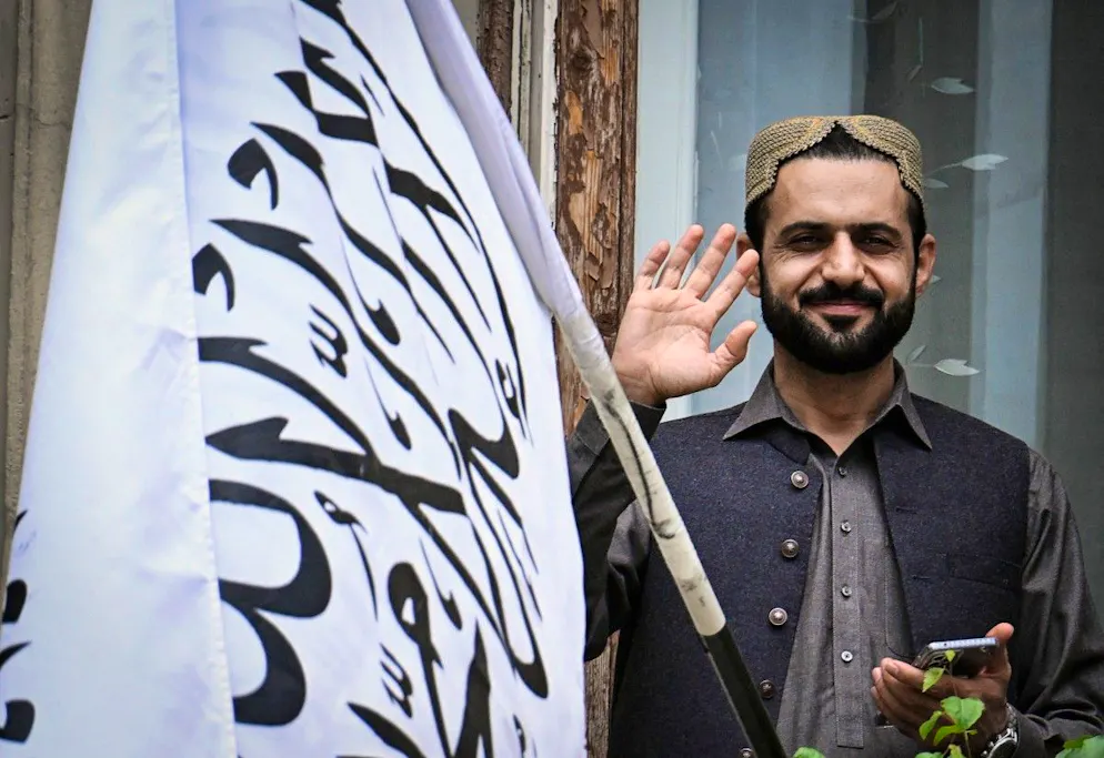 Un homme salue les passants, à côté du drapeau de l’Émirat islamique d’Afghanistan, depuis le balcon de l’ambassade afghane à Moscou, le 4 juillet 2025.