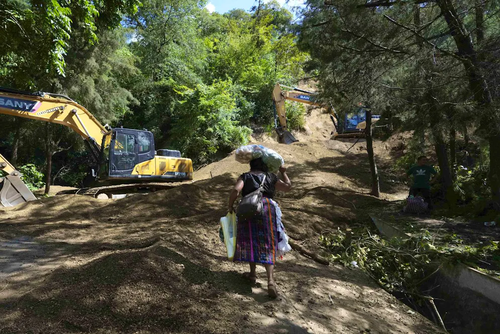 Une femme transporte de la nourriture alors qu'elle marche le long d'un glissement de terrain provoqué par des dizaines de tremblements de terre et de répliques enregistrés en quelques heures, à Santa Maria de Jesus, au Guatemala, le mercredi 9 juillet 2025. (AP Photo/Moises Castillo)