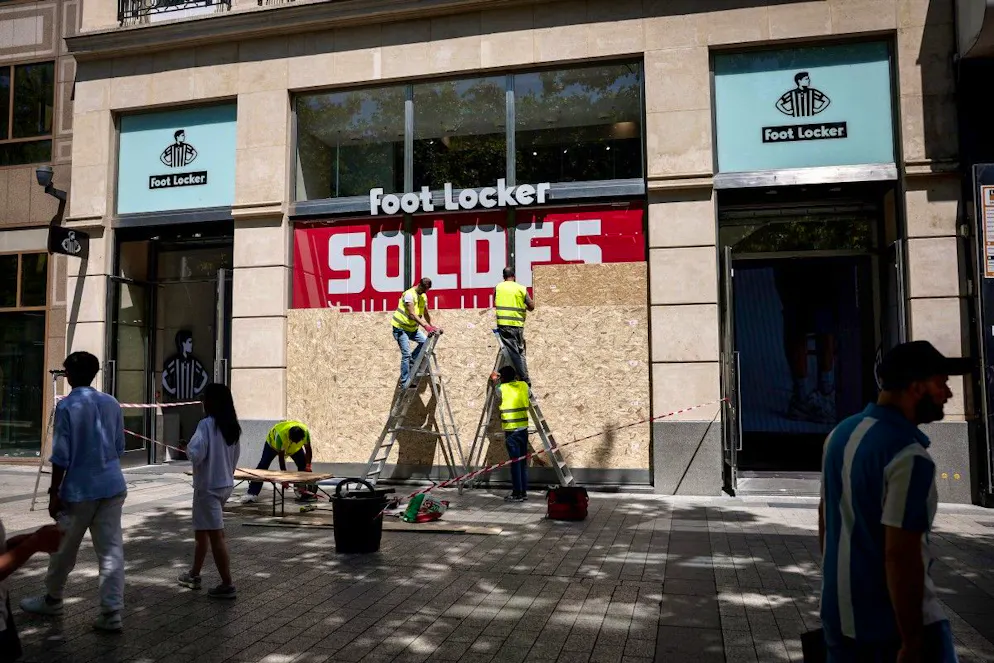 Des ouvriers recouvrent les vitrines d’un magasin Foot Locker avec des panneaux OSB pour les protéger d’éventuels dégâts ou pillages, à Paris, le 13 juillet 2025.