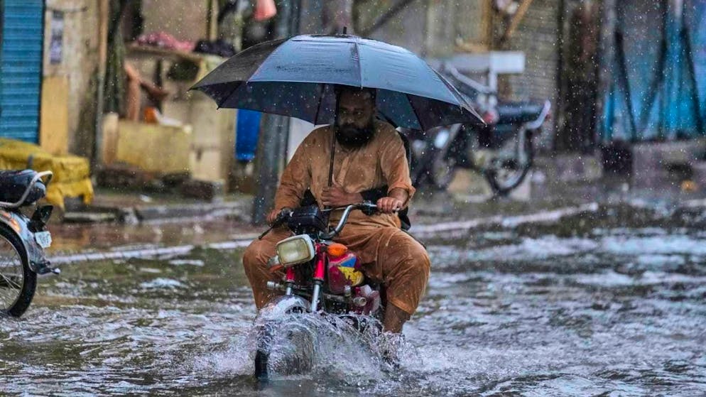 dpatopbilder - A motorcyclist with an umbrella rides through a flooded street in Rawalpindi. Photo: Anjum Naveed/AP/dpa