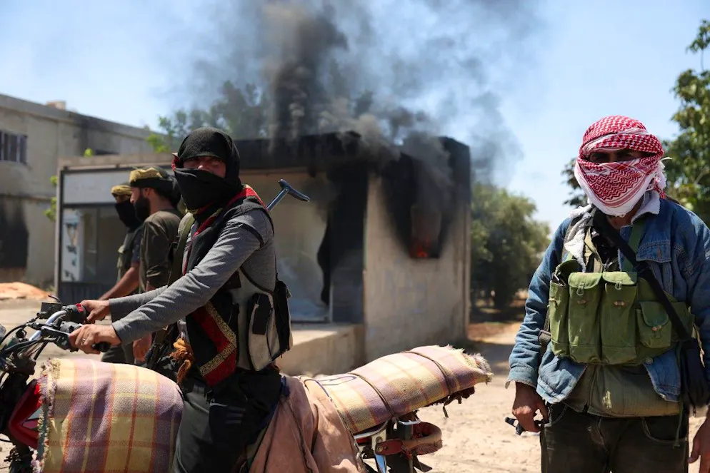 Des combattants issus de tribus bédouines se rassemblent près d'un bâtiment en feu dans le village d'al-Mazraa, dans le gouvernorat de Sweida, dans le sud de la Syrie, alors que les affrontements avec des hommes armés druzes se poursuivent le 18 juillet 2025.