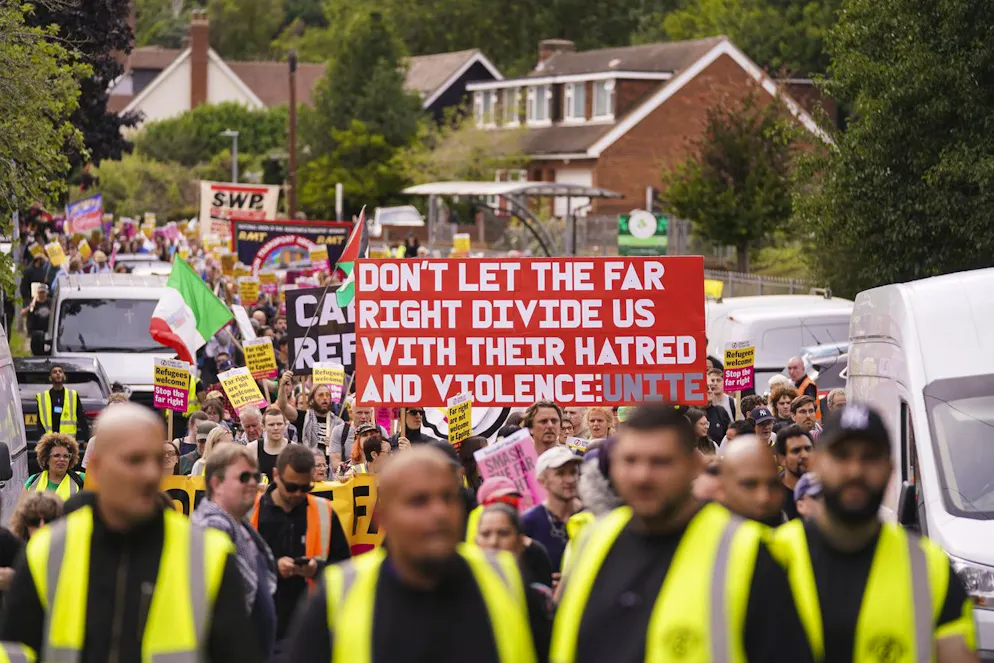 Des manifestants brandissent des pancartes et des banderoles alors qu'ils quittent une manifestation devant l'hôtel Bell à Epping, près de Londres, le dimanche 27 juillet 2025. (AP Photo/Alberto Pezzali)