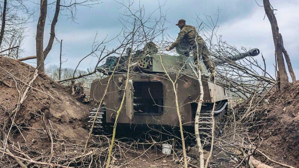 Un soldato ucraino copre con dei rami un veicolo blindato nel Donbass.