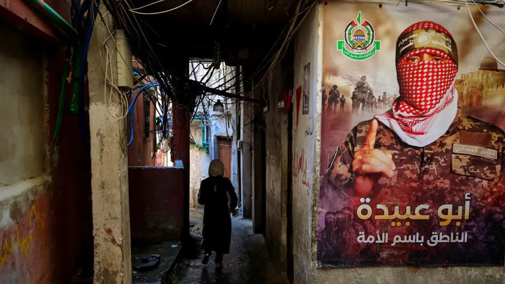ARCHIV - Ein palästinensischer Flüchtling geht durch eine enge Gasse im Beiruter Lager Burj el-Barjneh, in der ein Plakat von Abu Obeida, dem Sprecher der Kassam-Brigaden, hängt. Foto: Marwan Naamani/dpa (Archivbild)