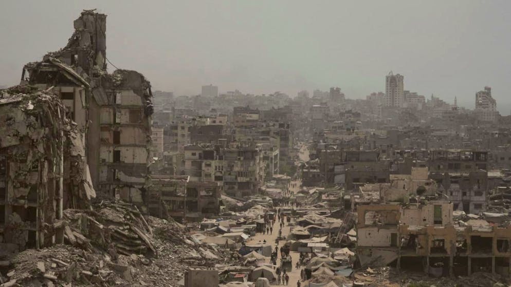 ARCHIV - Menschen gehen eine Straße entlang, die von Gebäuden umgeben ist, die durch israelische Bombardierungen im Gazastreifen zerstört wurden. Foto: Jehad Alshrafi/AP/dpa