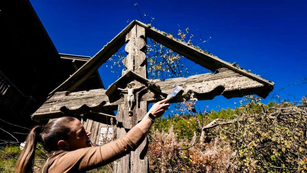 Blatten: les maisons épargnées nettoyées par plus de 70 bénévoles - Gallery. Une bénévole nettoie la boue qui recouvre la croix de Jésus dans le hameau de Weissenried, proche de Blatten.