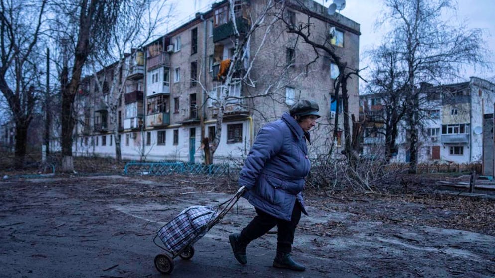 ARCHIV - Eine Einheimische geht zur Verteilungsstelle für humanitäre Hilfe vor einem Haus, das nach ukrainischen Angaben durch russischen Beschuss beschädigt wurde. Foto: Evgeniy Maloletka/AP/dpa