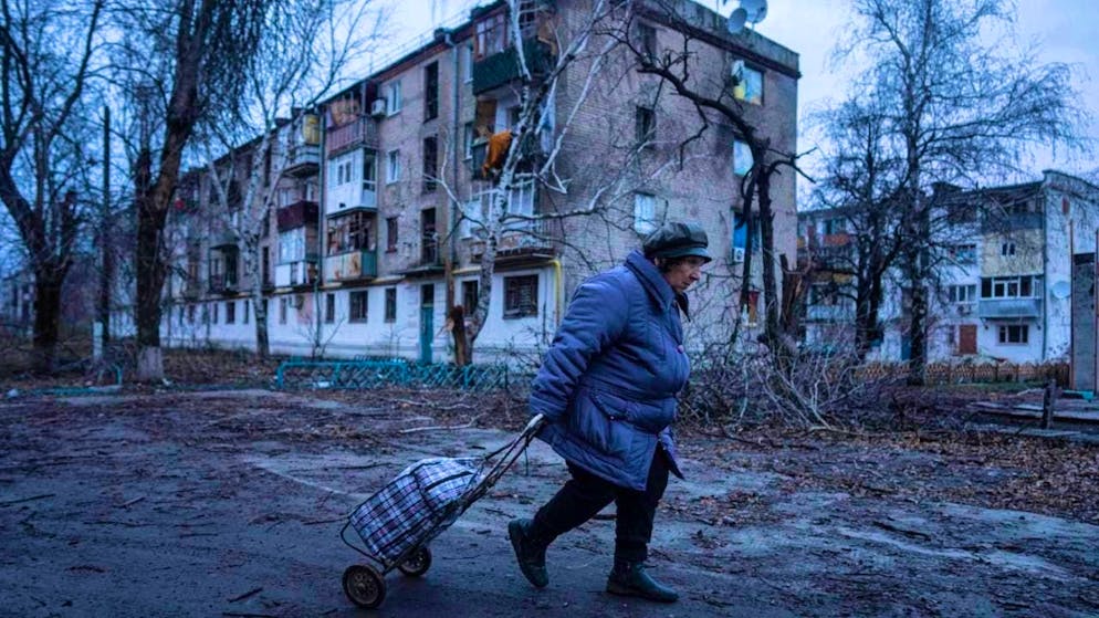 ARCHIVE - A local woman walks to the distribution point for humanitarian aid in front of a house which, according to Ukrainian sources, was damaged by Russian shelling. Photo: Evgeniy Maloletka/AP/dpa