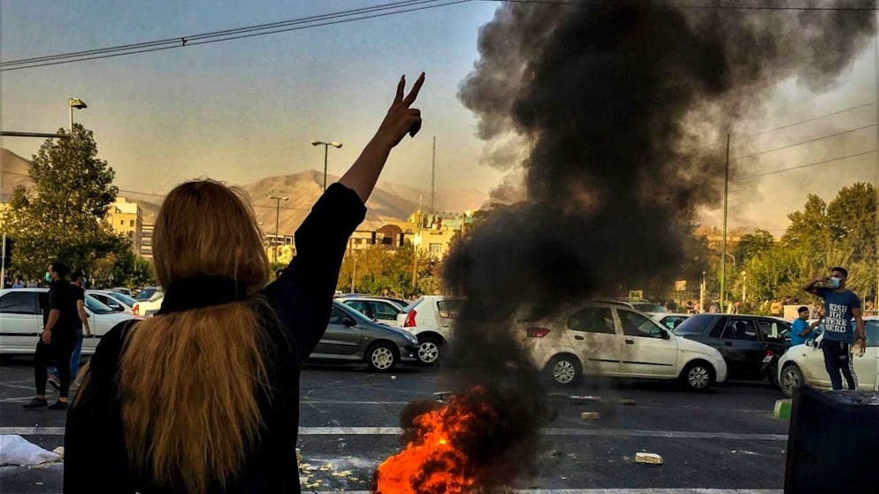 Eine Frau steht während einer Demonstration in Teheran vor einem brennenden Autoreifen und zeigt das Victory-Zeichen.
