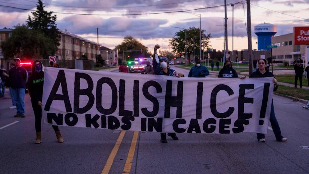 ARCHIV - Menschen halten ein Schild mit der Aufschrift "Abolish ICE" (ICE abschaffen), während die Polizei des Bundesstaates Illinois die Menge zurückdrängt. Foto: Adam Gray/AP/dpa