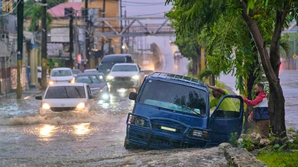 People leave a car on an impassable road flooded by the rains of Tropical Storm Melissa.