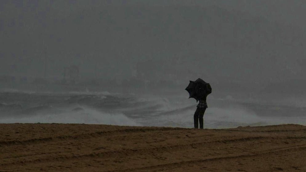 A visitor holds an umbrella on Ramakrishna beach in India. Photo: Mahesh Kumar A./AP/dpa