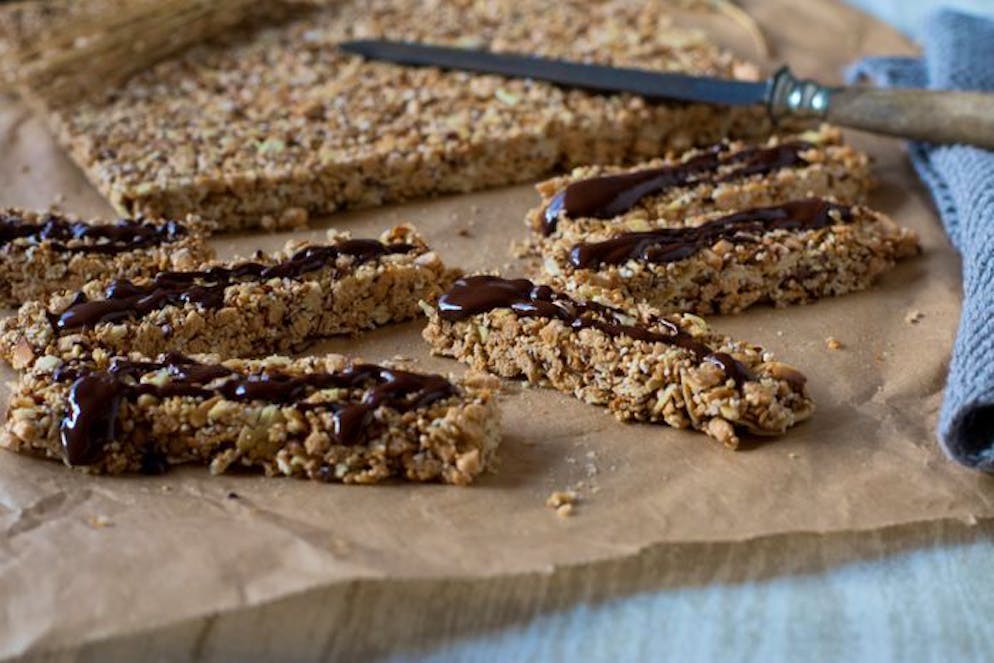 Damit startest du gesund in den Tag. Nach etwa zehn Minuten im Ofen die Nüsse und Samen mit einer Mischung aus 50 Gramm Honig, 50 Gramm Ahornsirup oder Dattelsüsse und 100 Gramm geschmolzenem Kokosöl verrühren. Danach die Mandel-Honig-Masse auf einem Blech mit Backpapier verteilen und für weitere 20 Minuten in den Ofen geben. Wenn das Blech abgekühlt ist, einzelne Riegel abschneiden und nach Wunsch mit dunkler Schokolade garnieren.