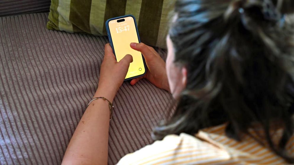 SYMBOLBILD - Eine Jugendliche liegt auf einem Sofa und entsperrt ihr Smartphone. Foto: Elisa Schu/dpa