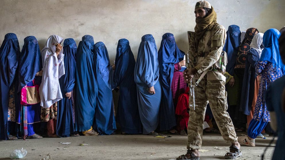 Ein Taliban-Kämpfer hält Wache, während Frauen in Kabul, Afghanistan, am 23. Mai 2023 darauf warten, Lebensmittelrationen von einer humanitären Organisation zu erhalten.