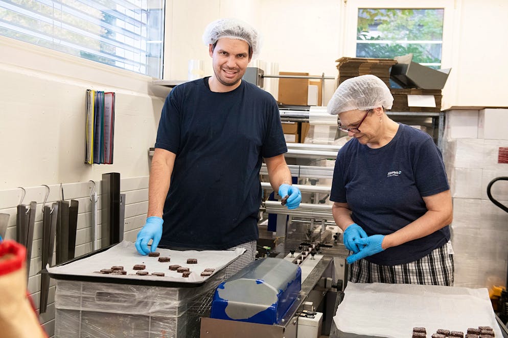 UBS Helpetica Backen. Vincent und Jacqueline verpacken die Brunsli einzeln mit einer Maschine.