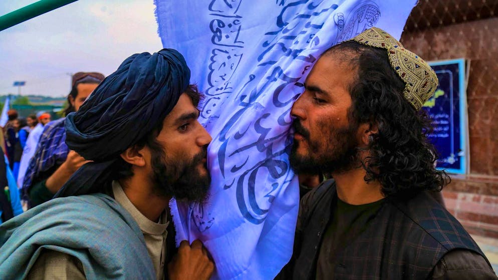 Membri dei Talebani baciano una bandiera del loro movimento durante un raduno vicino all'edificio dell'ex ambasciata statunitense a Kabul, in occasione del primo anniversario della loro presa di potere in Afghanistan, il 15 agosto 2022.