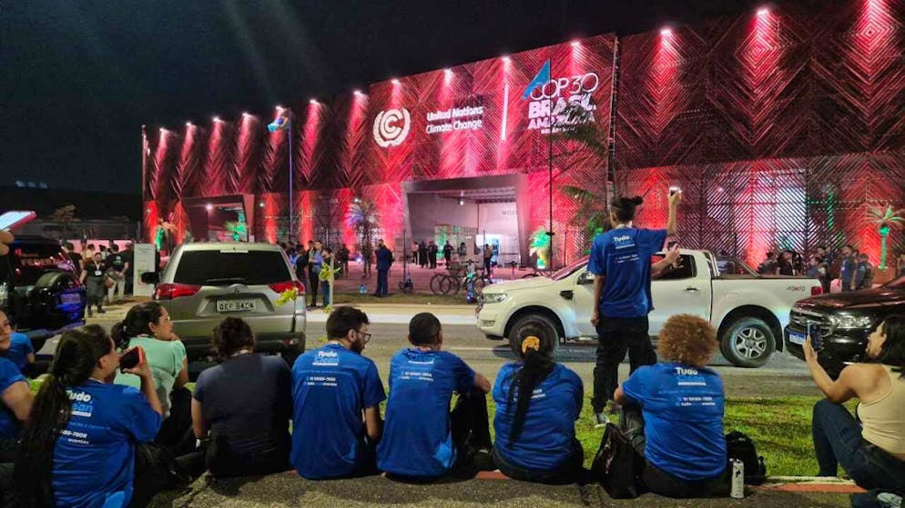 Reinigungskräfte sitzen vor dem Veranstaltungsort des UN-Klimagipfels COP30, nachdem Aktivisten dort eingedrungen waren und sie das Gelände verlassen mussten. Foto: Larissa Schwedes/dpa