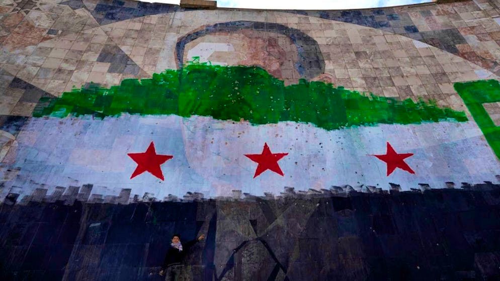 ARCHIVE - A Syrian boy stands under a huge portrait of the late Syrian President Al-Assad, painted over with the colors of the so-called "revolutionary" flag, in Damascus. Photo: Hussein Malla/AP/dpa/Symbolic image