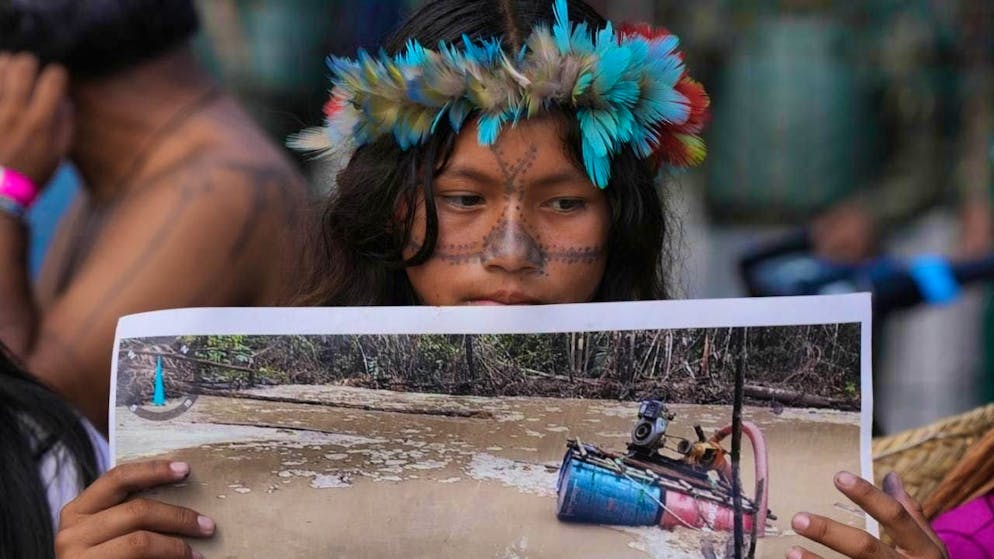 An indigenous woman holds a picture of a disaster as she demonstrates for the protection of the Amazon in front of the venue of the COP30 World Climate Conference. Photo: Fernando Llano/AP/dpa