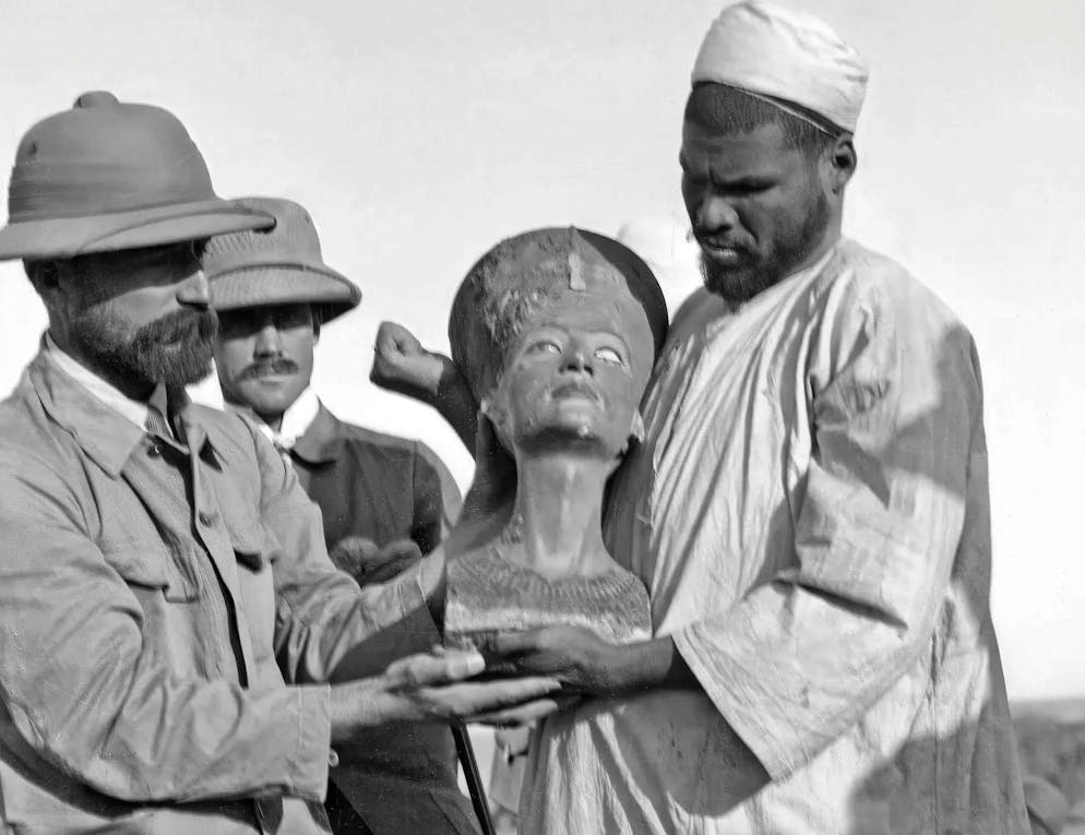 Néfertiti_Série d'images. Une des premières photos du buste de Néfertiti, peu après sa découverte à Tell el-Amarna en 1912, de gauche à droite : le superviseur des fouilles Herrmann Ranke, Paul Hollander et Mohammed es-Senussi.