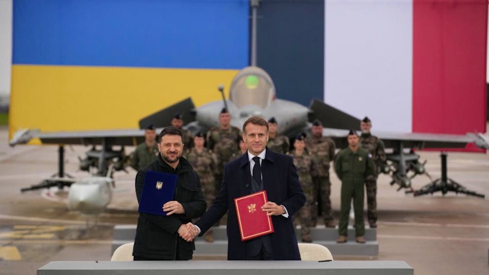 Der französische Präsident Emmanuel Macron (r) und der ukrainische Präsident Wolodymyr Selenskyj schütteln sich nach der Unterzeichnung eines Abkommens auf dem Luftwaffenstützpunkt Villacoublay bei Paris die Hände. Foto: Christophe Ena/Pool AP/dpa