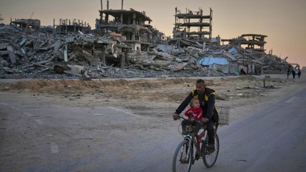 dpatopbilder - Ein Mann trägt ein Kind, während er mit dem Fahrrad eine beschädigte Straße im Lager Al-Shati entlangfährt. Foto: Jehad Alshrafi/AP/dpa
