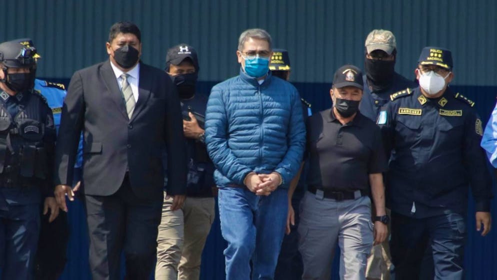 ARCHIV - Juan Orlando Hernandez (M), ehemaliger Präsident von Honduras, wird auf einem Luftwaffenstützpunkt in Handschellen zu einem wartenden Flugzeug gebracht. Knapp drei Monate nach dem Ende seiner Amtszeit ist der frühere Präsident von Honduras an die USA ausgeliefert worden. Foto: Elmer Martinez/AP/dpa