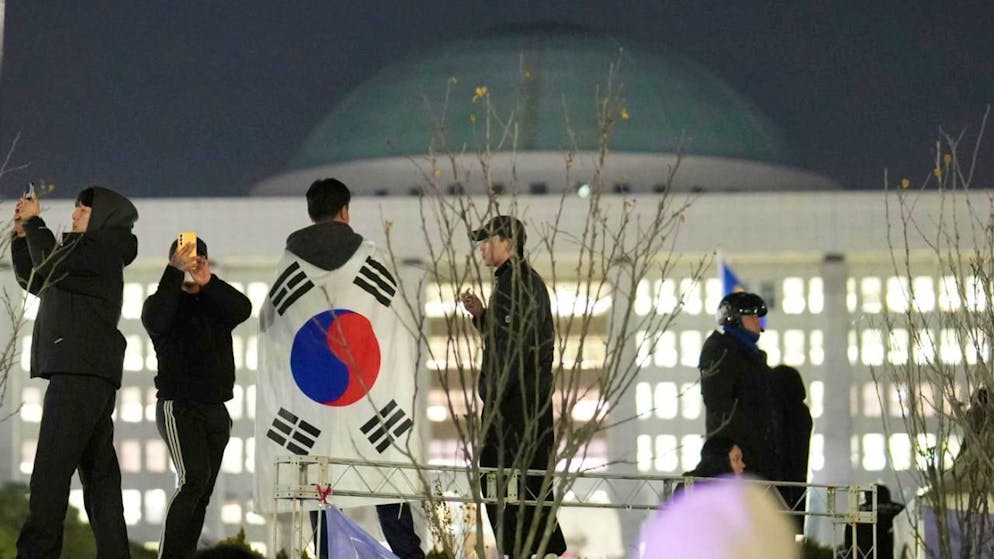 ARCHIV - Ein Mann mit einer Nationalflagge steht auf einer Mauer vor der Nationalversammlung. Der Präsident Südkoreas hat das Kriegsrecht ausgerufen. In einer live ausgestrahlten Rede beschuldigte er die Opposition des Landes, mit Nordkorea zu sympathisieren. Foto: Lee Jin-man/AP/dpa (Archivbild)
