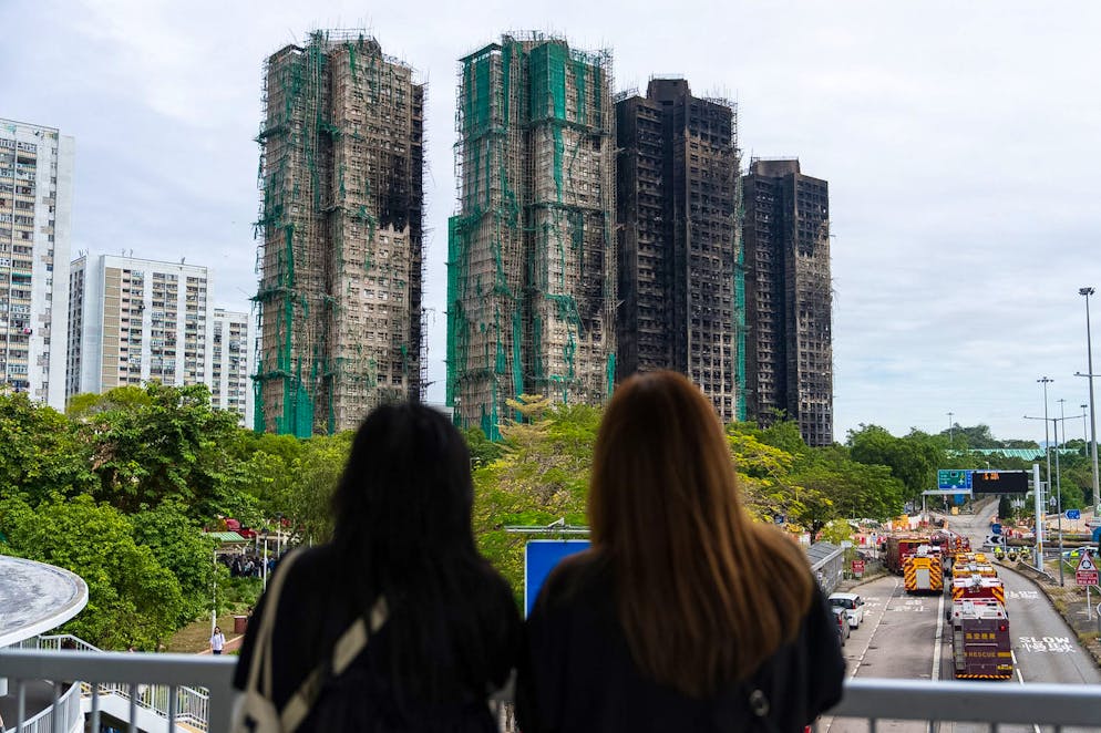 Alcune persone osservano gli edifici bruciati vicino al luogo dell'incendio mortale a Wang Fuk Court, un complesso residenziale nel distretto di Tai Po, nei Nuovi Territori di Hong Kong.