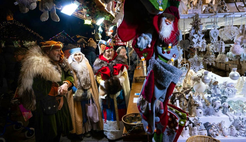Surtourism. Persone vestite con costumi medievali ammirano le decorazioni natalizie di uno stand del mercatino di Natale di Strasburgo.