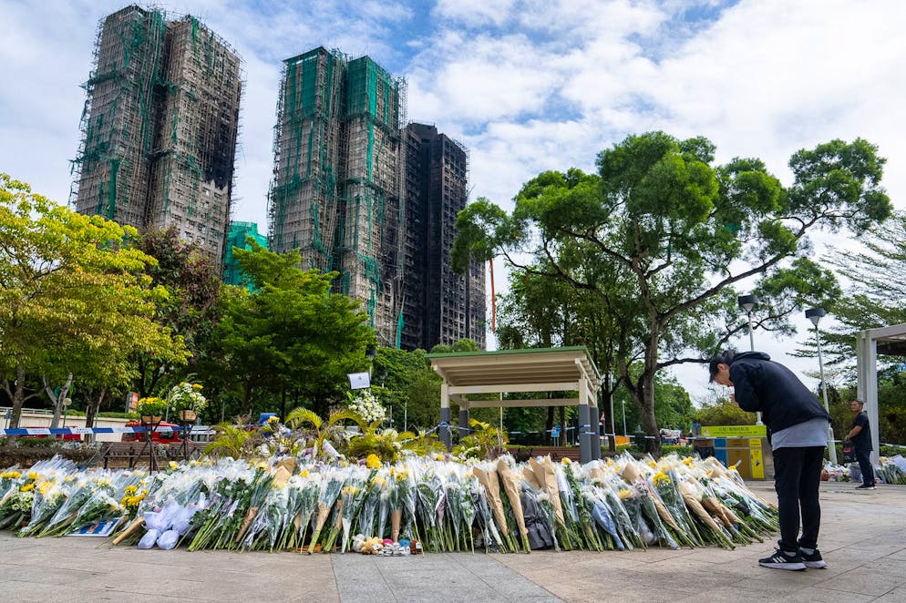 Des personnes déposent des fleurs en hommage aux victimes près du lieu où s'est déclaré un incendie meurtrier mercredi à Wang Fuk Court, un complexe résidentiel situé dans le district de Tai Po, dans les Nouveaux Territoires de Hong Kong, le lundi 1er décembre 2025. (AP Photo/Chan Long Hei)