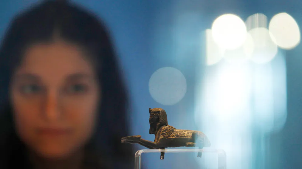 Psusennes_Tanis. Eine junge Frau betrachtet eine Miniatur-Sphinx aus der königlichen Nekropole von Tanis. Das Kleinod stammt aus einem Königsgrab in Tanis und wurde von Pierre Montet ausgegraben.