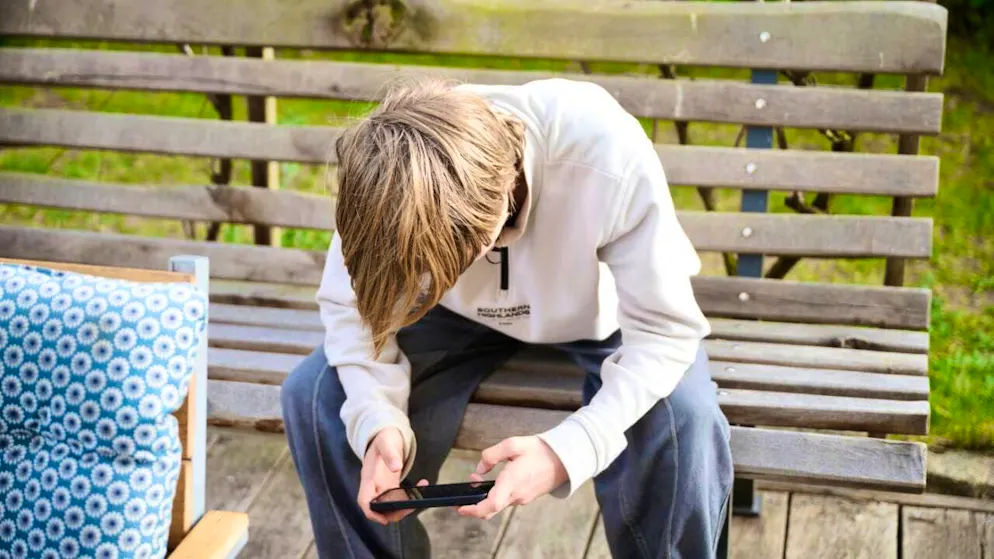 ILLUSTRATION - A teenager sits on a bench and looks at his smartphone. Australia has introduced a social media ban for children and young people under the age of 16, making it a global pioneer. (to dpa: "Australia: Social media ban for under-16s starts") Photo: Annette Riedl/dpa - ATTENTION: For editorial use only in connection with the above text