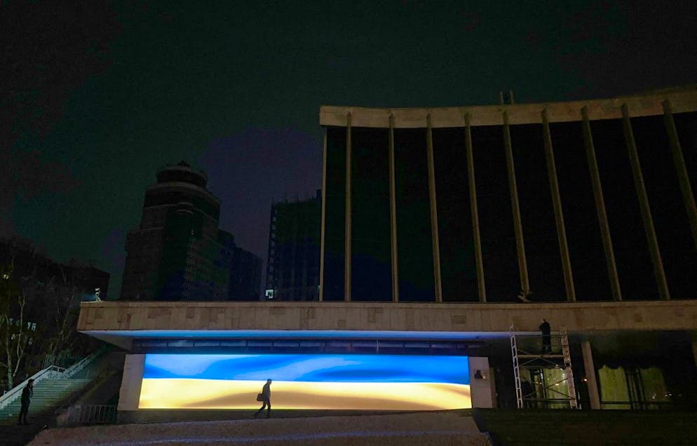 Un piéton passe devant un écran affichant le drapeau national ukrainien pendant les heures de coupure de courant à Kyiv, le 11 décembre 2025. 