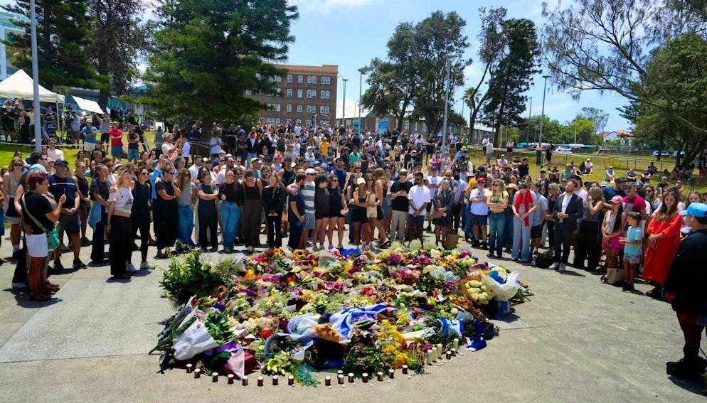 Le persone si riuniscono intorno a un monumento floreale sulla spiaggia di Bondi Beach, a Sydney, il giorno dopo la sparatoria.