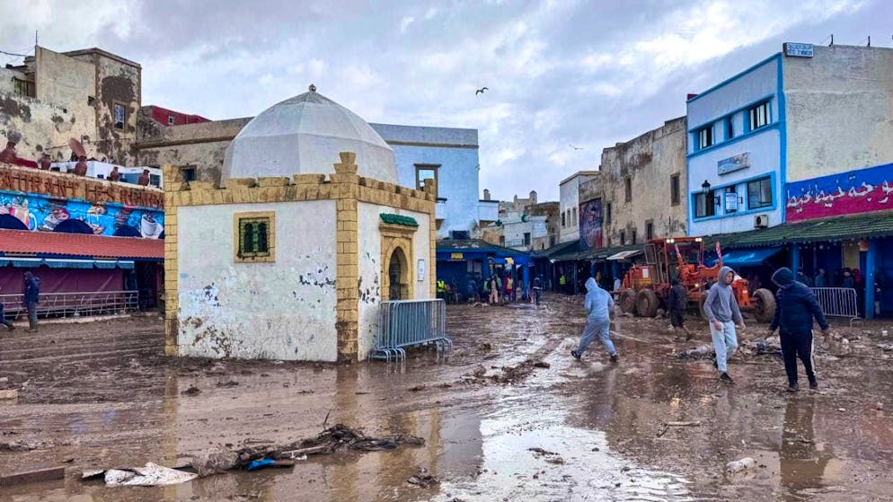 People walk along a road covered in mud. At least 37 people have died in Morocco after heavy rainfall and flooding. Photo: Abderrazak Gouach/AP/dpa