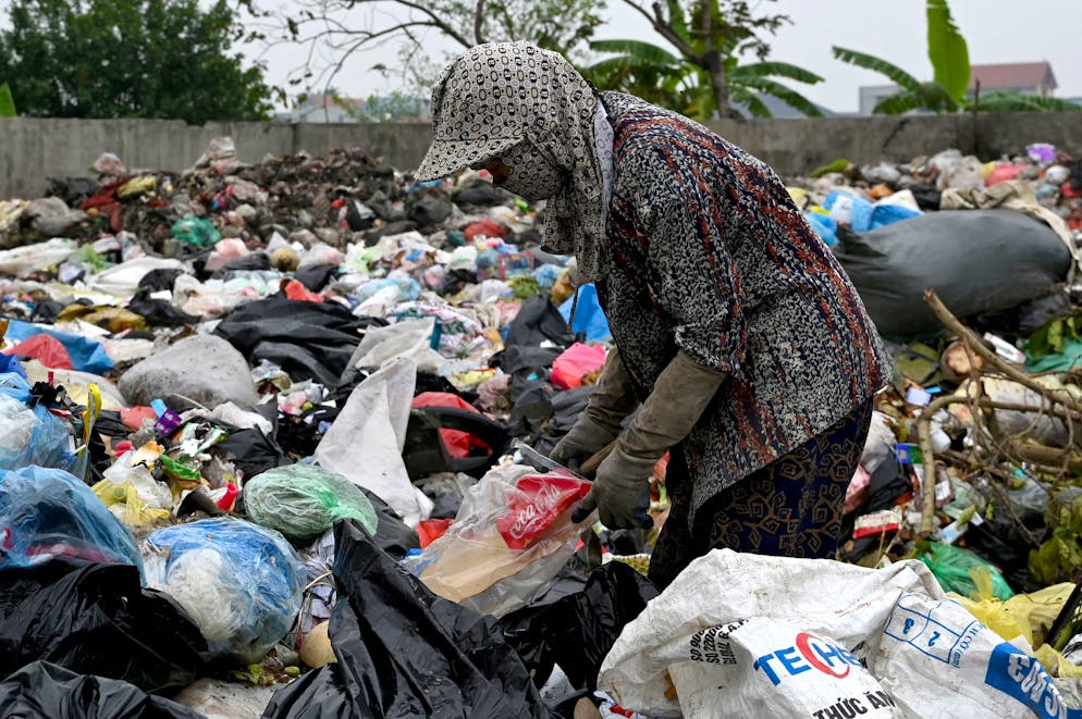 Cette photo prise le 11 décembre 2025 montre une femme triant des déchets plastiques dans une décharge à la périphérie de Hanoï. Accroupie entre des montagnes de plastique jeté, Lanh enlève les étiquettes des bouteilles de Coca-Cola, d'Evian et de boissons au thé vietnamiennes locales afin qu'elles puissent être fondues en petits granulés pour être réutilisées. (Photo de Nhac NGUYEN / AFP) / À ACCOMPAGNER DE « VIETNAM-ENVIRONNEMENT-SANTÉ-PLASTIQUE-RECYCLAGE » FOCUS PAR TRAN THI MINH HA, LAM NGUYEN ET TY MCCORMICK