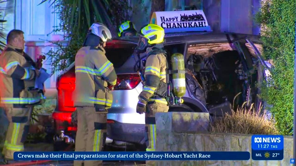 A screenshot from an ABC News livestream video shows firefighters responding to a vehicle fire in St Kilda East. A sign with the words "Happy Chanukah!" (Happy Hanukkah) can be seen on the roof of the fire-damaged car parked in the driveway outside the rabbi's home. Photo: Abc News/ABC NEWS/AAP Image/dpa - ATTENTION: For editorial use only in connection with current reporting and only with full attribution to the above credit